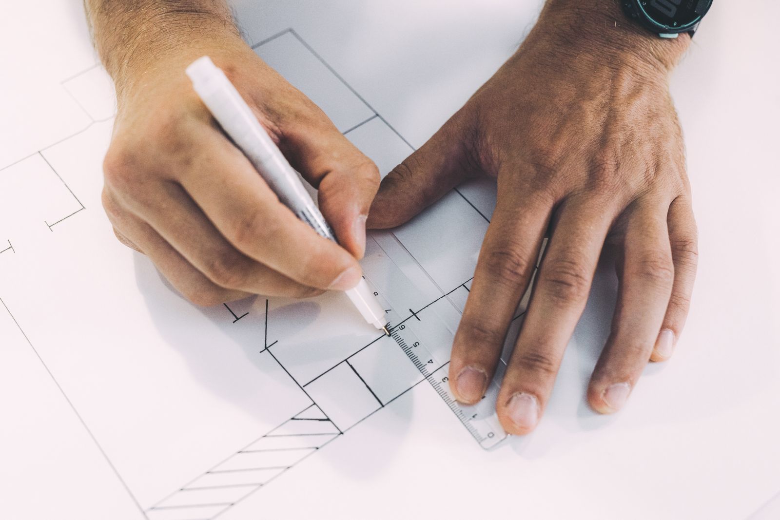 Hands drawing a bathroom setting-out plan with a ruler and pen.